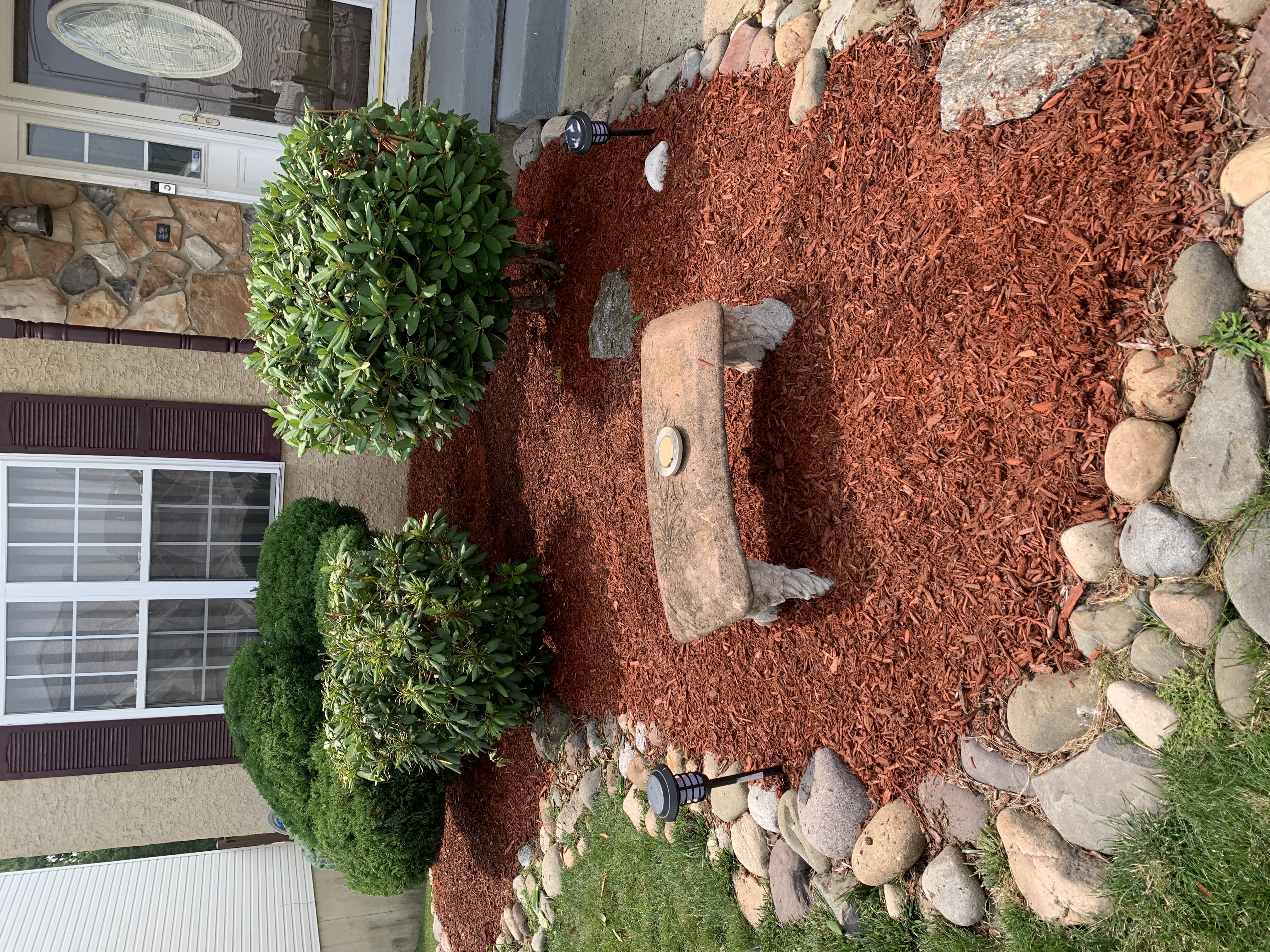 Close-up of red mulch bed with stone mushroom accent and river rock