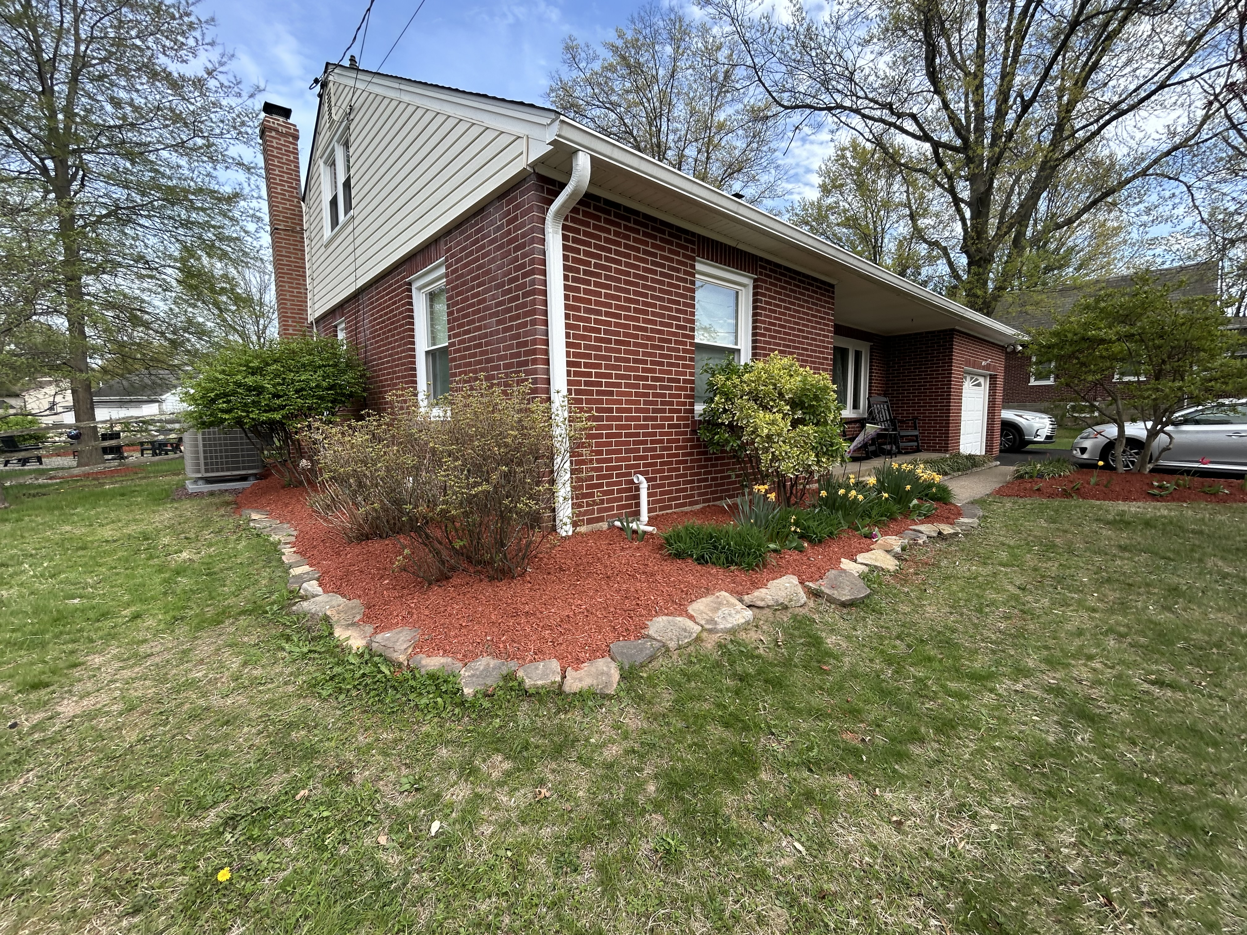 Corner foundation bed with red mulch and natural stone border