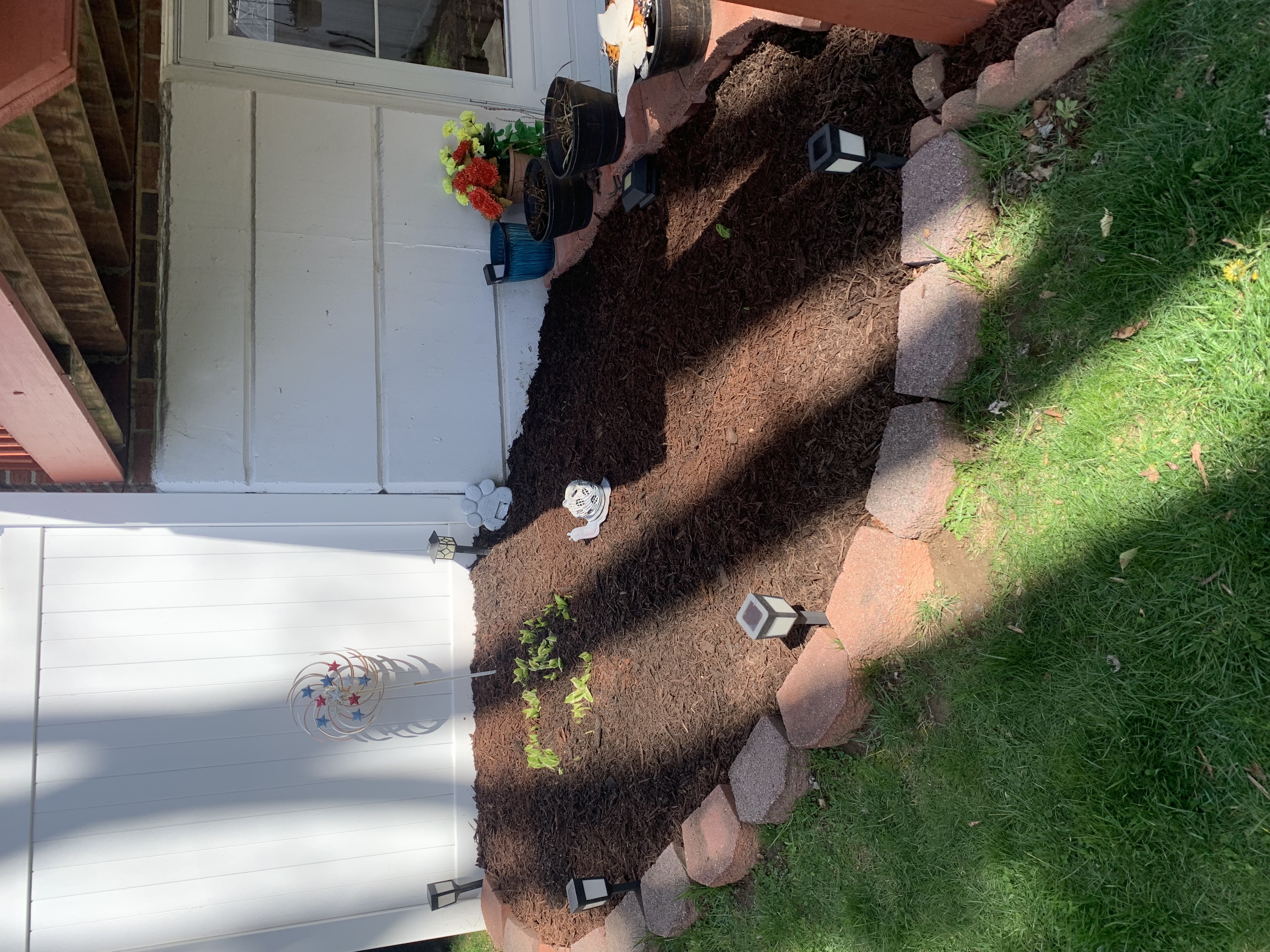 Side bed with brown mulch, solar lights, and stone border